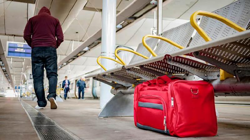 Individual walking away from a red duffle bag left under airport seats
