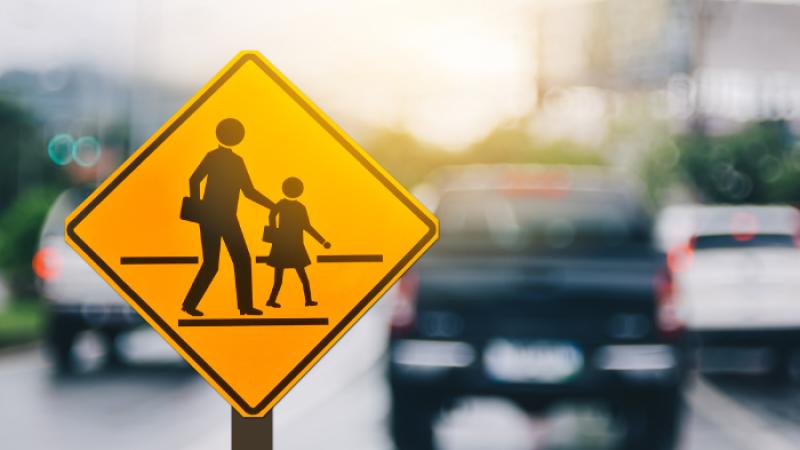 School crossing sign in front of blurred out cars in the background