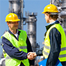 Chemical Partnerships Two men wearing hard hats and bright yellow-green vests shaking hands at a chemical facility.