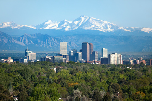 The Denver, Colorado skyline with the trees of City Park in the foreground and Longs and Meeker peaks in the background. Peaks are snowccapped.