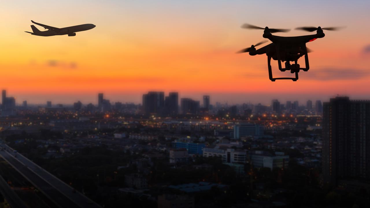 A drone flying at dusk near an aircraft over a city
