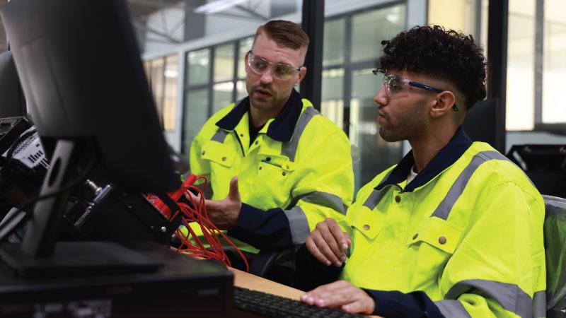 Two technical students wearing safety gear while learning to work on equipment