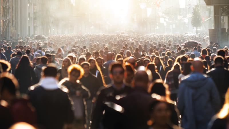 Image of a large group of people walking outdoors in a city block setting