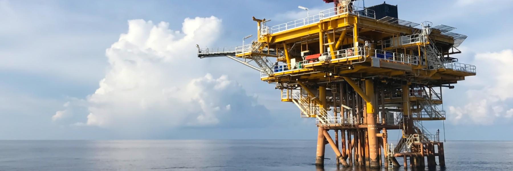 an oil rig out in the ocean with blue sky and white clouds in the background